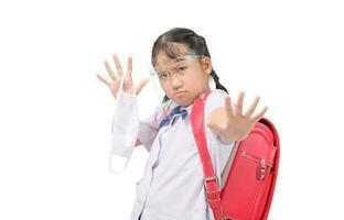 weinig Aziatisch leerling meisje vervelend schild gezicht en houdt een kleding masker tegen besmettelijk virus en tonen hou op handen gebaar foto