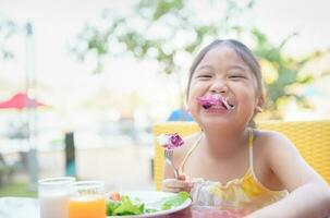 schattig weinig meisje aan het eten vers groenten en salade Aan ochtend. foto