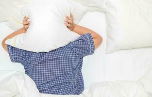 zwaarlijvig dik jongen aan het liegen in bed aan het bedekken hoofd met hoofdkussen foto