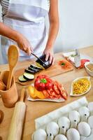 vrouw koken snijdend aubergine Aan houten bord in keuken. foto