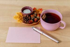 herfst humeur samenstelling Aan een houten tafel met thee beker, groet kaart en bladeren. foto