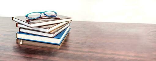 stack van boeken met lezing bril Aan houten bureau. onderwijs spandoek. foto