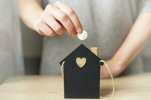 dames hand- Holding een munt in de buurt weinig speelgoed- huis . huis spaargeld concept foto