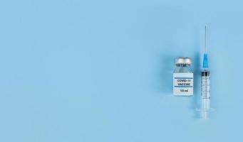 spuit voor eenmalig gebruik en medische fles met coronavirusvaccin op blauwe achtergrond met kopie ruimte foto