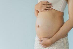 zwanger vrouw houdt handen Aan buik en pastel kleur achtergrond. zwangerschap, moederschap, voorbereiding en verwachting concept. detailopname, kopiëren ruimte. jong vrouw aan het wachten voor baby geboorte. foto