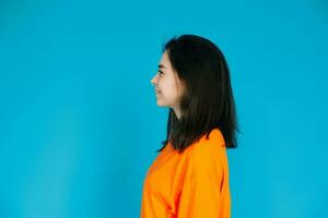 stralend jong vrouw in elegant oranje kleding glimlachen met een stralend getand glimlach, profiel portret, geïsoleerd Aan blauw achtergrond foto