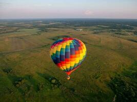 een kleurrijk lucht ballon is vliegend in vrij vlucht over- de veld. vogelperspectief visie. multi gekleurde ballon in de blauw lucht foto