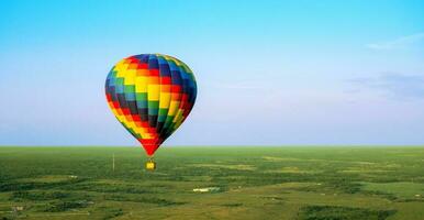 een kleurrijk lucht ballon is vliegend in vrij vlucht over- de veld. vogelperspectief visie. multi gekleurde ballon in de blauw lucht foto