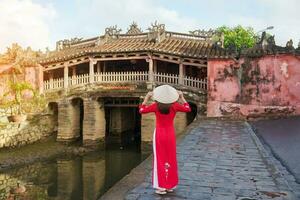 vrouw reiziger vervelend oa dai Vietnamees jurk bezienswaardigheden bekijken Bij Japans gedekt brug in Hoi een dorp, Vietnam. mijlpaal en populair voor toerist attracties. Vietnam en zuidoosten Azië reizen concept foto