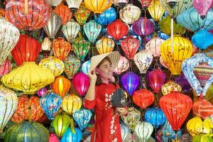 gelukkig vrouw vervelend oa dai Vietnamees jurk met kleurrijk lantaarns, reiziger bezienswaardigheden bekijken Bij Hoi een oude stad- in centraal vietnam.landmark voor toerist attracties.vietnam en zuidoosten reizen concept foto