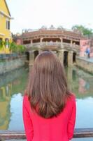 vrouw reiziger vervelend oa dai Vietnamees jurk bezienswaardigheden bekijken Bij Japans gedekt brug in Hoi een dorp, Vietnam. mijlpaal en populair voor toerist attracties. Vietnam en zuidoosten Azië reizen concept foto