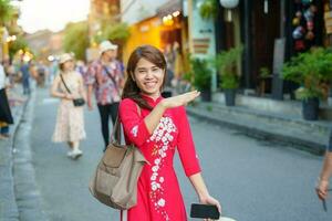 gelukkig vrouw vervelend oa dai Vietnamees jurk, Aziatisch reiziger bezienswaardigheden bekijken Bij Hoi een oude stad- in centraal Vietnam. mijlpaal en populair voor toerist attracties. Vietnam en zuidoosten reizen concept foto