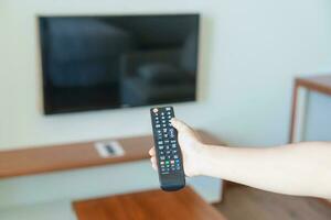 hand- gebruik makend van afgelegen controleur voor aanpassen slim TV binnen de modern kamer Bij huis. appartement leven concept foto