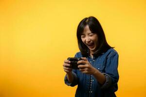 portret jong Aziatisch vrouw met gelukkig succes glimlach vervelend denim kleren Holding bedieningshendel controleur en spelen video spel. pret en kom tot rust hobby vermaak levensstijl concept. foto