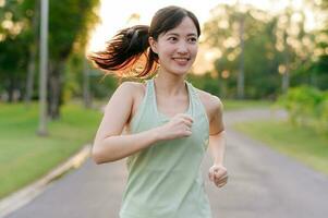 fit Aziatisch jong vrouw jogging in park glimlachen gelukkig rennen en genieten van een gezond buitenshuis levensstijl. vrouw jogger. geschiktheid loper meisje in openbaar park. gezond levensstijl en welzijn wezen concept foto