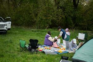 gelukkig jong familie, vier kinderen hebben pret en genieten van buitenshuis Aan picknick deken schilderij Bij tuin voorjaar park, ontspanning. foto