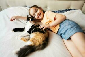 schattig weinig meisje aan het liegen Aan de bed met haar kat Bij huis foto