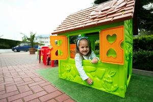 weinig meisje spelen in groen plastic kind huis Bij kinderen speelplaats. kind hebben pret buitenshuis. foto