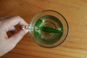 hennep thee in glas kop en hand- vangst kop Aan licht bruin tafel. vers groen een deel van hennep blad in thee. top visie. foto