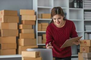 beginnend klein bedrijf ondernemer van onafhankelijk Aziatisch vrouw glimlachen gebruik makend van computer laptop met vrolijk succes van online afzet pakket doos items en mkb levering concept foto