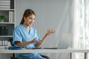 Aziatisch dokter jong mooi vrouw glimlachen gebruik makend van werken met een laptop computer en haar schrijven iets Aan papierwerk of klembord wit papier Bij ziekenhuis bureau kantoor, gezondheidszorg medisch concept foto