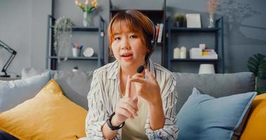 Aziatische zakenvrouw die laptop gebruikt, praat met collega's over het plan in een videogesprek terwijl ze vanuit huis in de woonkamer werkt