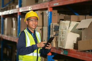 Aziatisch magazijn fabriek mannetje manager gelukkig gebruik makend van digitaal tablet communicatie gereedschap in een magazijn terwijl staand Aan een plank op zoek Bij de camera foto