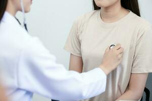 Aziatisch vrouw dokter in uniform Holding een stethoscoop en gebruik makend van het naar meten de hart tarief van een Aziatisch vrouw geduldig met hart ziekte foto