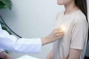 Aziatisch vrouw dokter in uniform Holding een stethoscoop en gebruik makend van het naar meten de hart tarief van een Aziatisch vrouw geduldig met hart ziekte foto