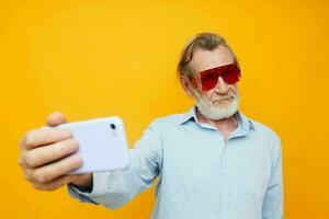 ouderen Mens in rood bril met telefoon geel achtergrond foto