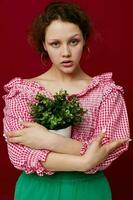 aantrekkelijk jong vrouw stand-in en Holding bloem in pot rood achtergrond foto