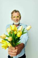 senior grijs haar Mens een boeket van bloemen met bril net zo een geschenk licht achtergrond foto