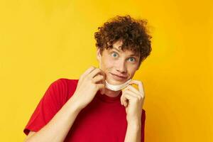 vent met rood gekruld haar- vervelend een rood t-shirt medisch masker Aan de gezicht poseren geel achtergrond ongewijzigd foto