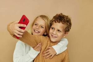 foto van twee kinderen in truien poseren voor pret met telefoon geïsoleerd achtergrond