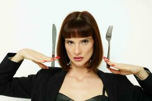 mooi vrouw in een zwart jasje een mes en een vork in de buurt de gezicht licht achtergrond foto