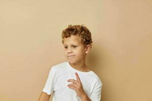 vrolijk jongen met gekruld haar- in een wit t-shirt beige achtergrond foto