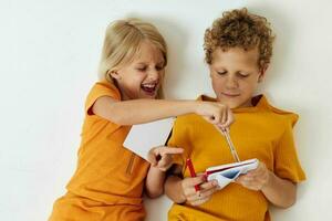 twee blij kinderen liggen Aan de verdieping met blocnotes en potloden geïsoleerd achtergrond ongewijzigd foto