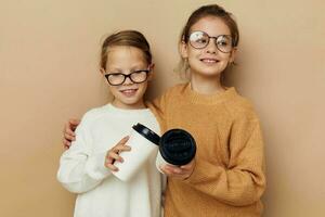 twee weinig grappig meisjes een glas met een drinken beige achtergrond foto