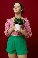 aantrekkelijk jong vrouw in roze blouse is poseren met een fabriek in wit pot foto