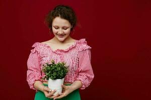 vrolijk meisje in een roze blouse pot met een bloem in haar handen rood achtergrond foto