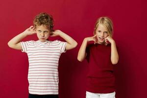 schattig peuter- kinderen glimlachen en poseren in gewoontjes kleren tegen rood achtergrond foto