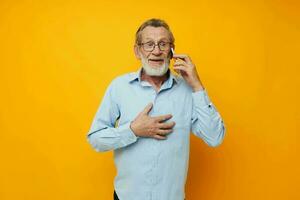 portret van gelukkig senior Mens grijs baard met bril pratend Aan de telefoon geel achtergrond foto