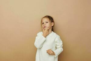 schattig meisje in wit trui poseren hand- gebaren beige achtergrond foto