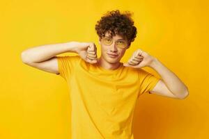 portret van een jong gekruld Mens geel t-shirt bril mode hand- gebaren geïsoleerd achtergrond ongewijzigd foto