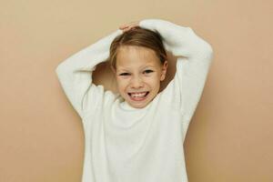 portret van gelukkig glimlachen kind meisje in wit trui poseren hand- gebaren beige achtergrond foto