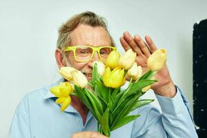 oud Mens in een blauw overhemd met een boeket van bloemen licht achtergrond foto