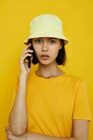 optimistisch jong vrouw in een geel hoed jeugd stijl gewoontjes pratend Aan de telefoon levensstijl ongewijzigd foto