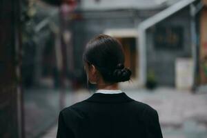 elegant vrouw in een zwart jasje wandelingen langs de stad straat met haar terug naar de camera, volgen me foto