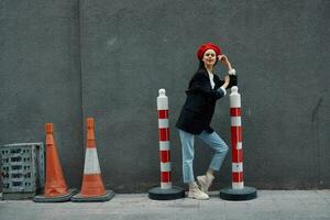 mode vrouw staand leunend tegen een muur straat tegen een achtergrond van de stad weg werken toerist in elegant kleren met rood lippen en rood baret, reis, filmische kleur, retro wijnoogst stijl. foto