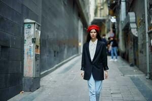 mode vrouw portret wandelen toerist in elegant kleren met rood lippen en rood baret wandelen naar beneden een versmallen stad straat, reis, filmische kleur, retro wijnoogst stijl. foto